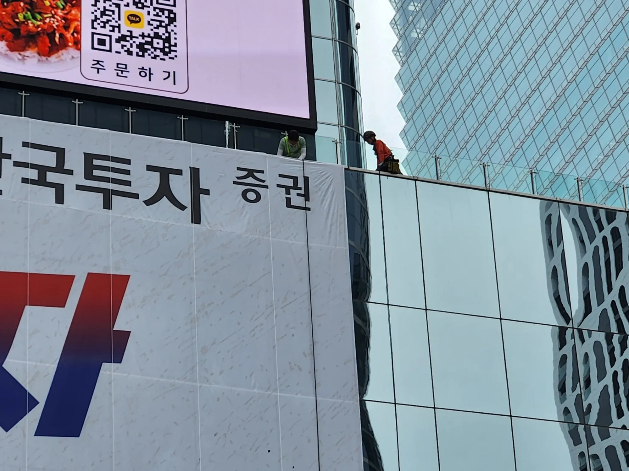 고층 건물 외벽 응원 현수막 상단에서 마무리 고정 작업을 하는 기술자 2명